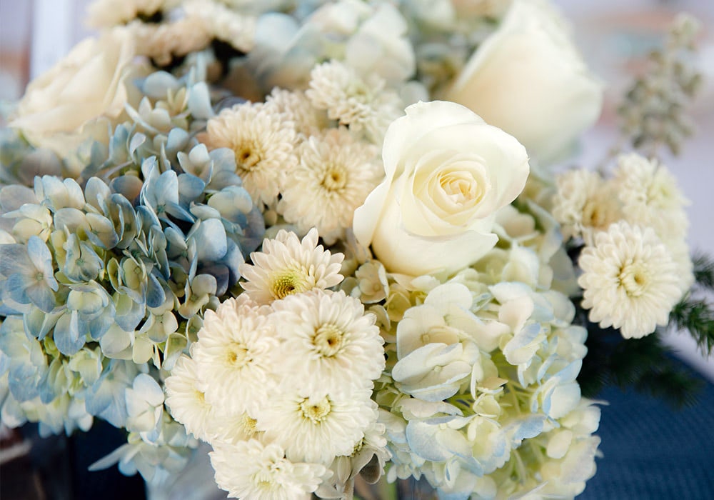 A bouquet of white roses, pale blue hydrangeas, and white chrysanthemums, arranged closely together, creating an elegant and fresh floral display.